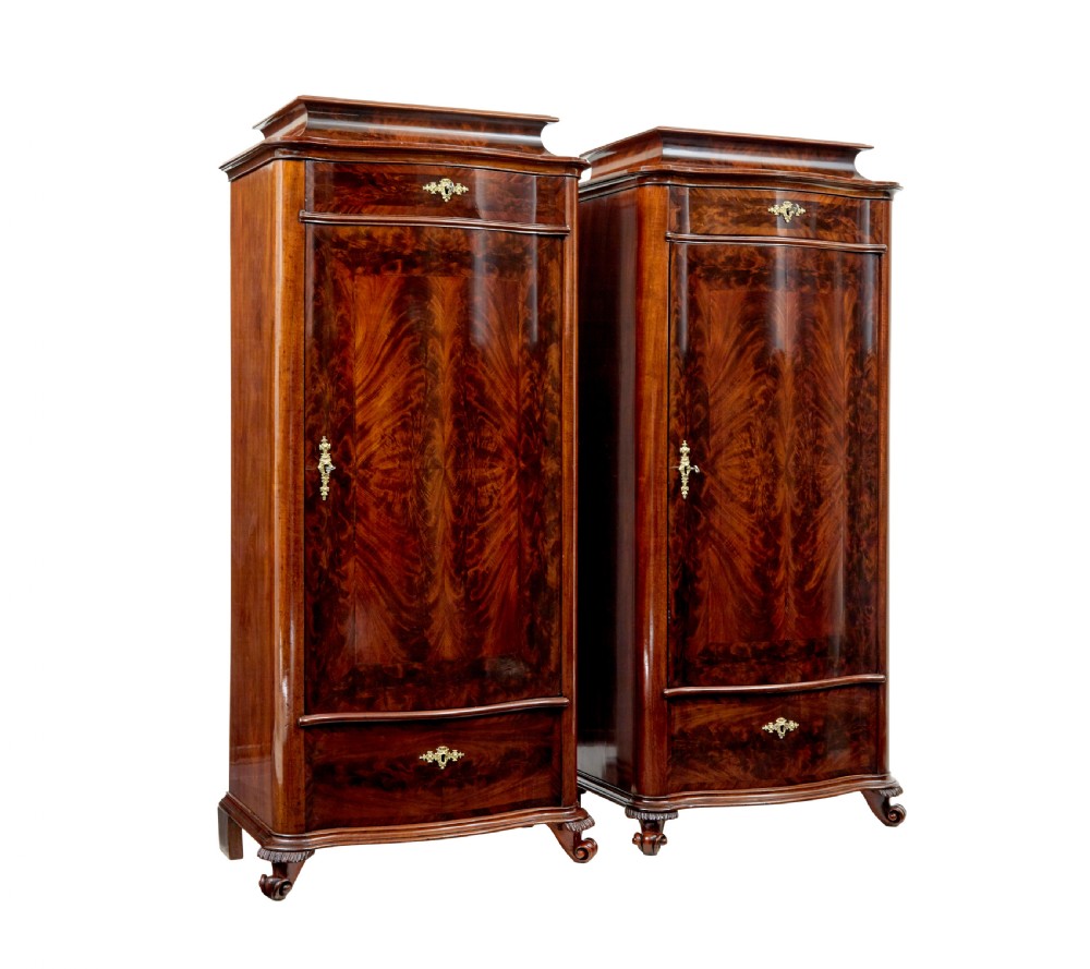 A pair of 19th-century Scandinavian tall mahogany cupboards featuring serpentine fronts, flame veneer panels, and ornate brass keyhole escutcheons.