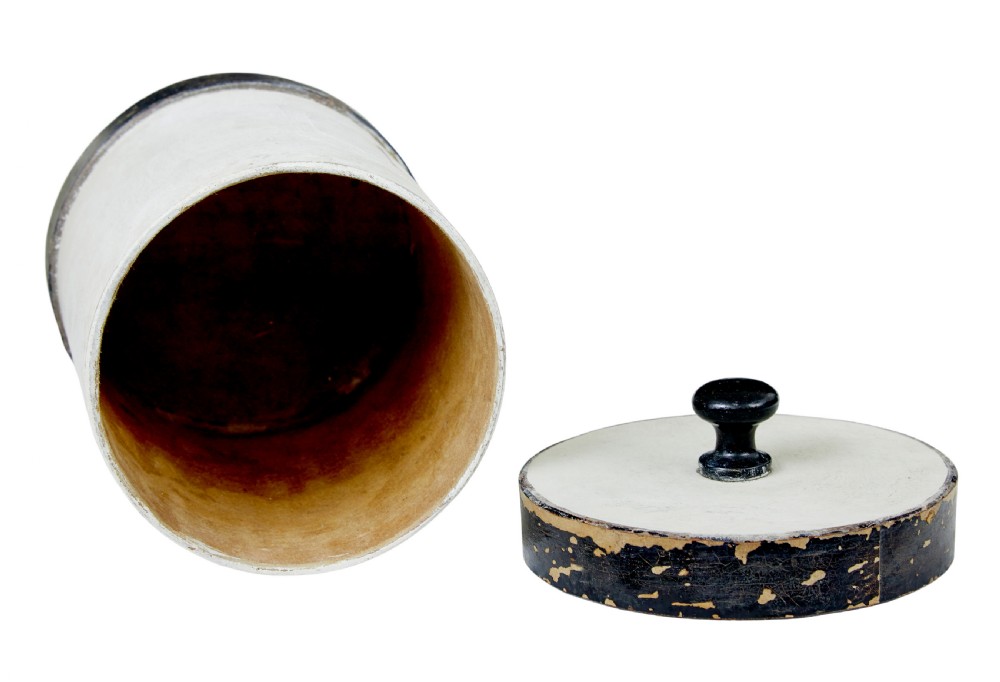 A set of eight cylindrical off-white painted wooden jars with black bases, black rims, turned black lid knobs, and painted rectangular label borders. View VI