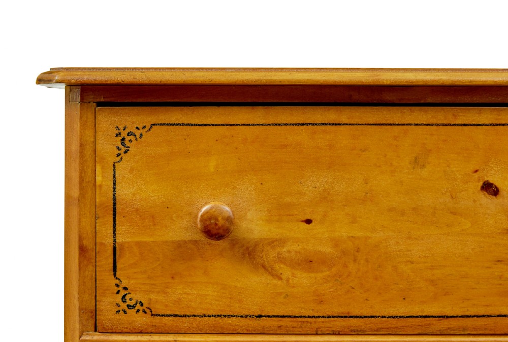 A tall Swedish honey-coloured wooden chest of four drawers featuring hand-painted black corner flourishes and turned knobs. View IV