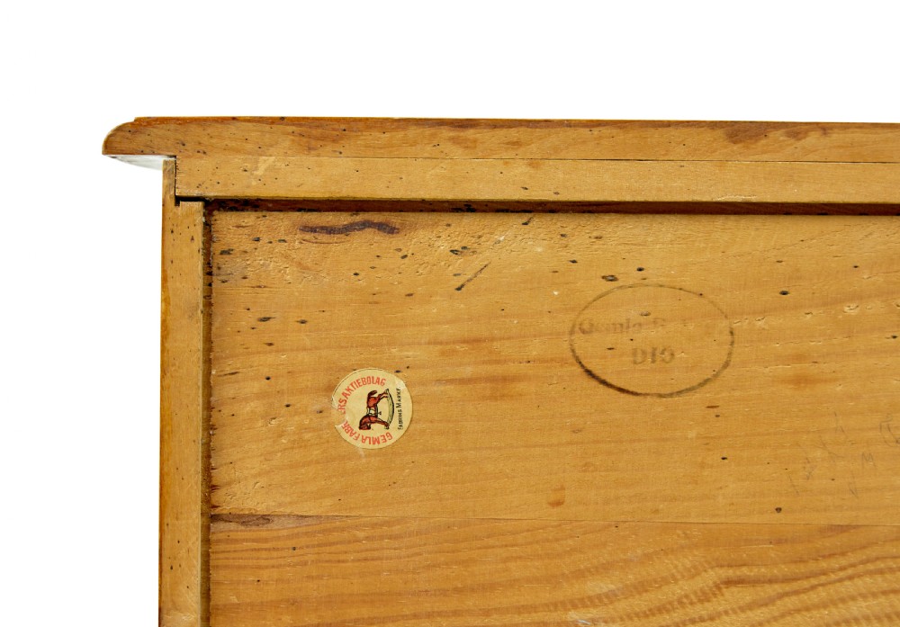 A tall Swedish honey-coloured wooden chest of four drawers featuring hand-painted black corner flourishes and turned knobs. View V