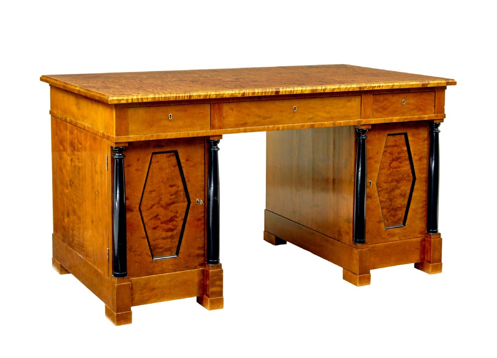 A Swedish Empire Revival pedestal desk crafted from golden flame birch veneer featuring three frieze drawers, ebonised column accents, and geometric inlaid cabinet doors.