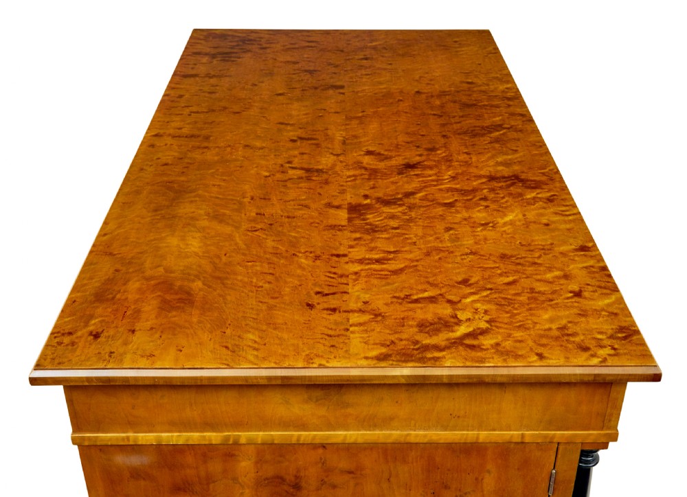 A Swedish Empire Revival pedestal desk crafted from golden flame birch veneer featuring three frieze drawers, ebonised column accents, and geometric inlaid cabinet doors. View X