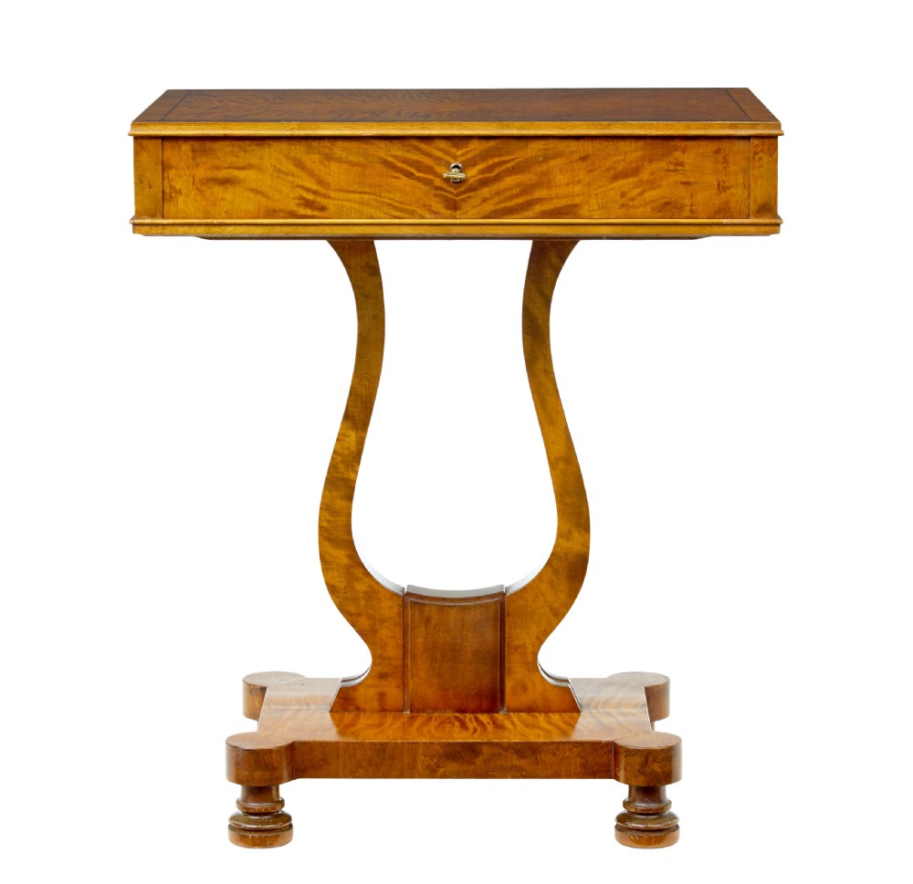 A late nineteenth-century warm golden birch sewing table featuring a single drawer with a brass keyhole, supported by a lyre-shaped pedestal on a plinth base with bun feet.