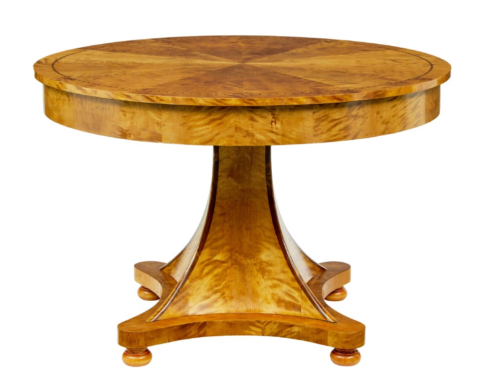 A circular golden flame birch centre table featuring a starburst-patterned veneer top, decorative inlaid rim border, sweeping concave pedestal stem, and quadform base with bun feet.