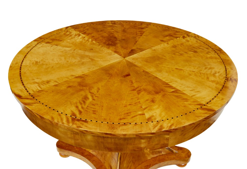 A circular golden flame birch centre table featuring a starburst-patterned veneer top, decorative inlaid rim border, sweeping concave pedestal stem, and quadform base with bun feet. View III