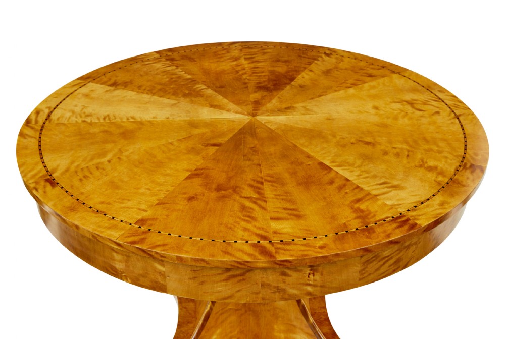 A circular golden flame birch centre table featuring a starburst-patterned veneer top, decorative inlaid rim border, sweeping concave pedestal stem, and quadform base with bun feet. View IV