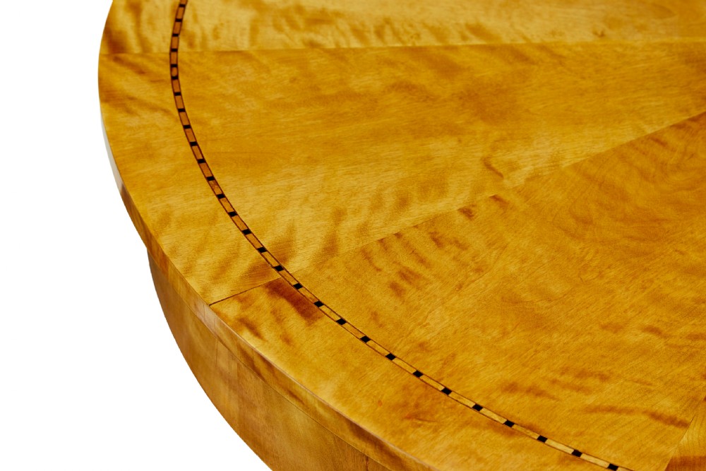 A circular golden flame birch centre table featuring a starburst-patterned veneer top, decorative inlaid rim border, sweeping concave pedestal stem, and quadform base with bun feet. View V