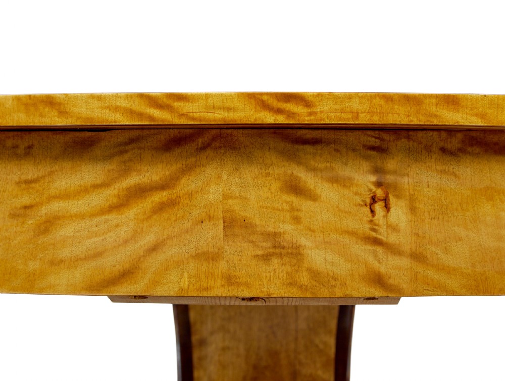 A circular golden flame birch centre table featuring a starburst-patterned veneer top, decorative inlaid rim border, sweeping concave pedestal stem, and quadform base with bun feet. View IX