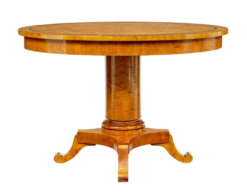 A late 19th-century Swedish circular centre table in golden satin birch veneer, featuring ebonised inlay, a cylindrical pedestal column, and a four-point plinth with scroll feet.