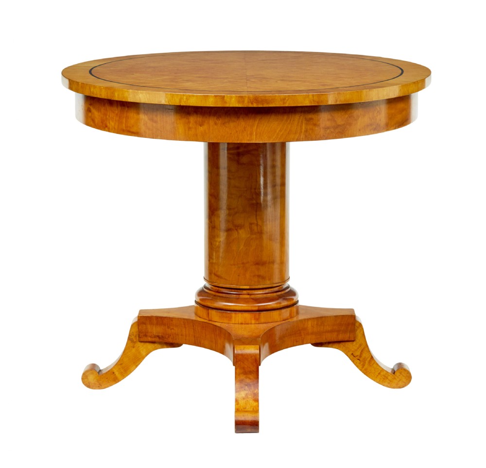 A late 19th-century Swedish circular centre table in golden satin birch veneer, featuring ebonised inlay, a cylindrical pedestal column, and a four-point plinth with scroll feet. View II