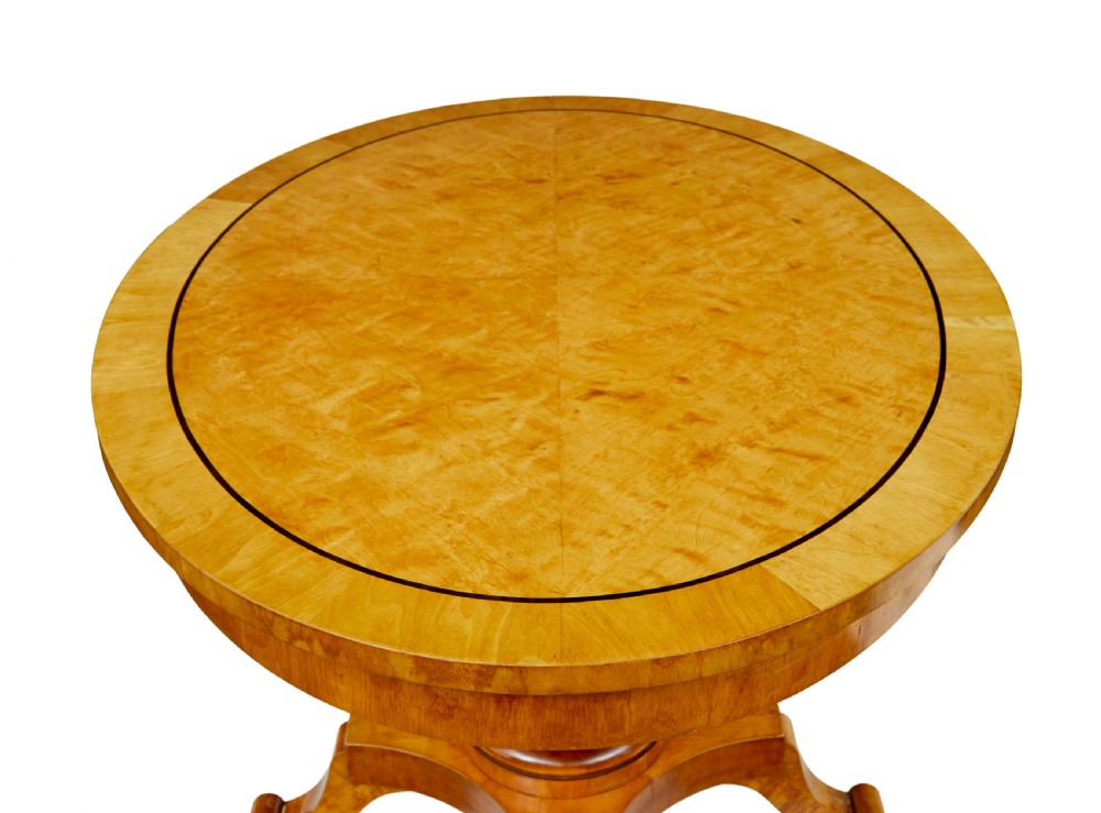 A late 19th-century Swedish circular centre table in golden satin birch veneer, featuring ebonised inlay, a cylindrical pedestal column, and a four-point plinth with scroll feet. View V