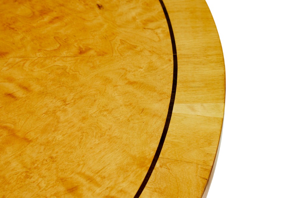 A late 19th-century Swedish circular centre table in golden satin birch veneer, featuring ebonised inlay, a cylindrical pedestal column, and a four-point plinth with scroll feet. View VI