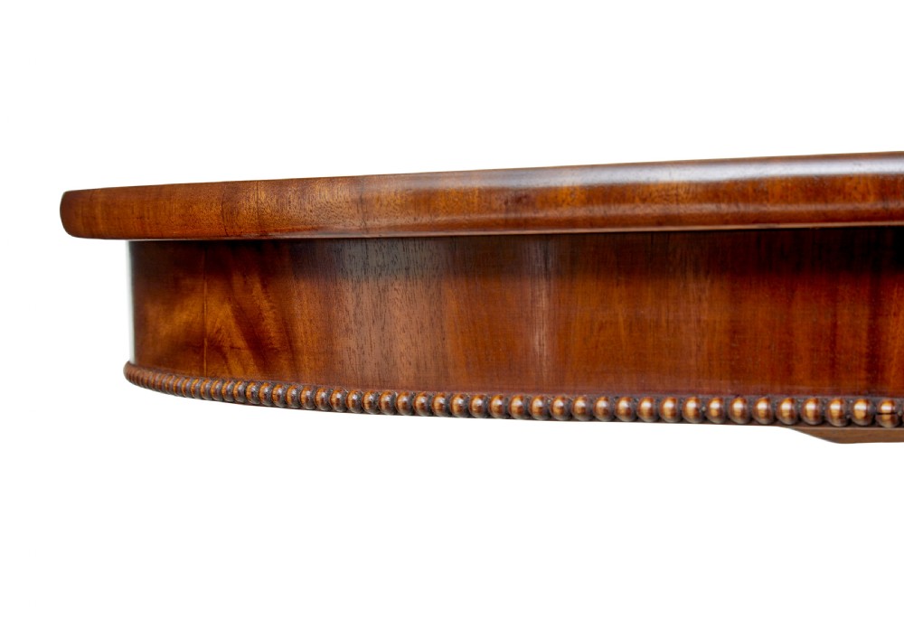 A 19th-century oval wood centre table featuring a flame mahogany veneered top, beaded apron moulding, turned central column, and carved scroll feet. View VI