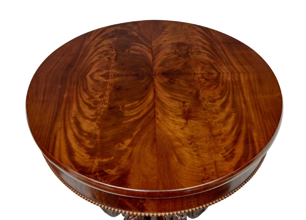A 19th-century oval wood centre table featuring a flame mahogany veneered top, beaded apron moulding, turned central column, and carved scroll feet. View VIII