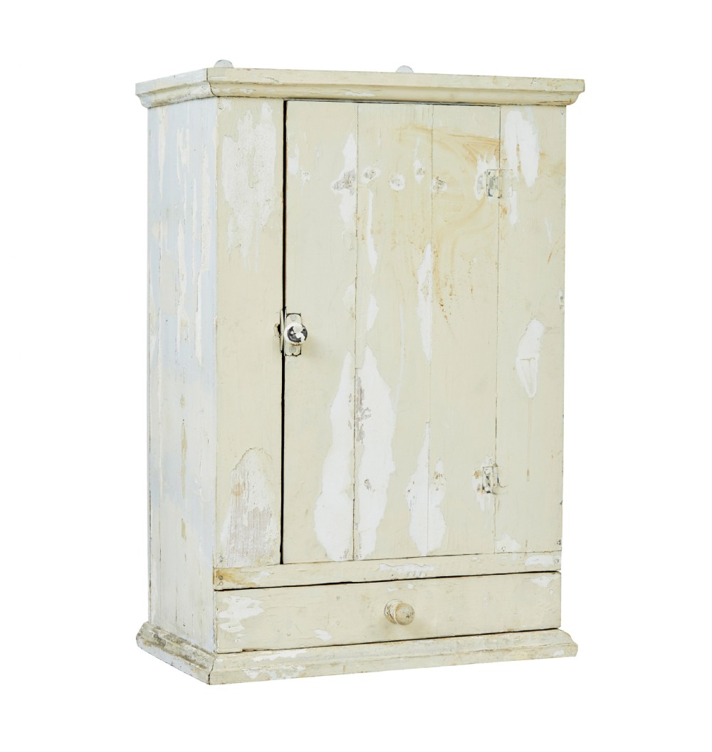 A 19th-century Scandinavian pine wall cupboard with a distressed cream painted finish, a single panelled door, and one lower drawer.