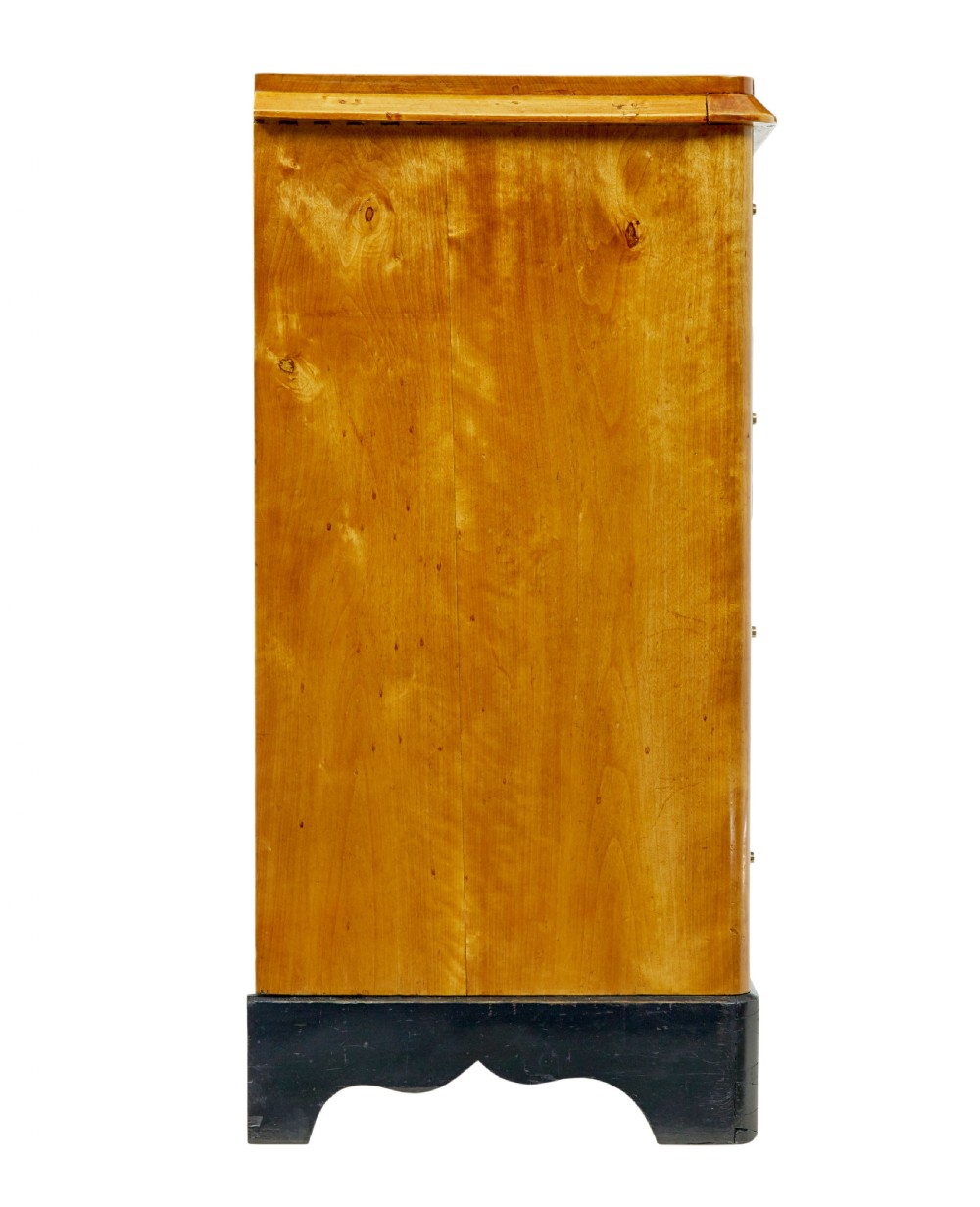 A 19th-century Swedish Empire Revival birch chest of drawers featuring four graduated drawers with metal handles, keyhole escutcheons, and a dark ebonised plinth base. View VI