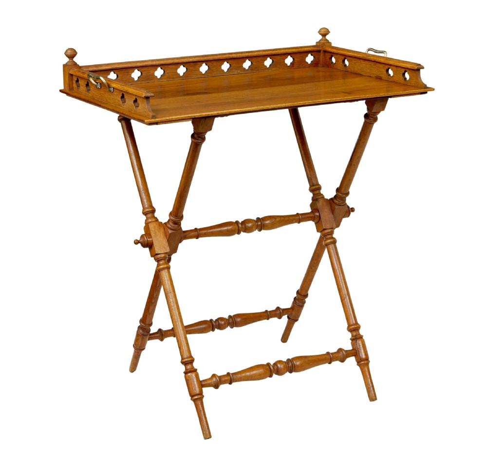 A 19th-century oak butlers tray featuring a trefoil pierced gallery border and brass handles resting on a folding X-frame stand.