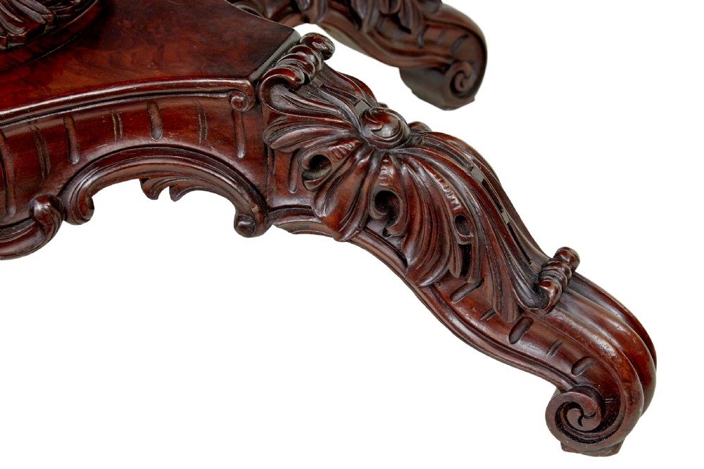 An antique 19th-century oval mahogany centre table featuring a carved apron, a central turned pedestal stem, and a carved four-legged base with scroll feet. View VII