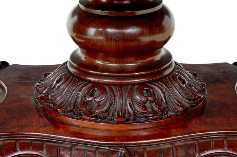 An antique 19th-century oval mahogany centre table featuring a carved apron, a central turned pedestal stem, and a carved four-legged base with scroll feet. View VIII
