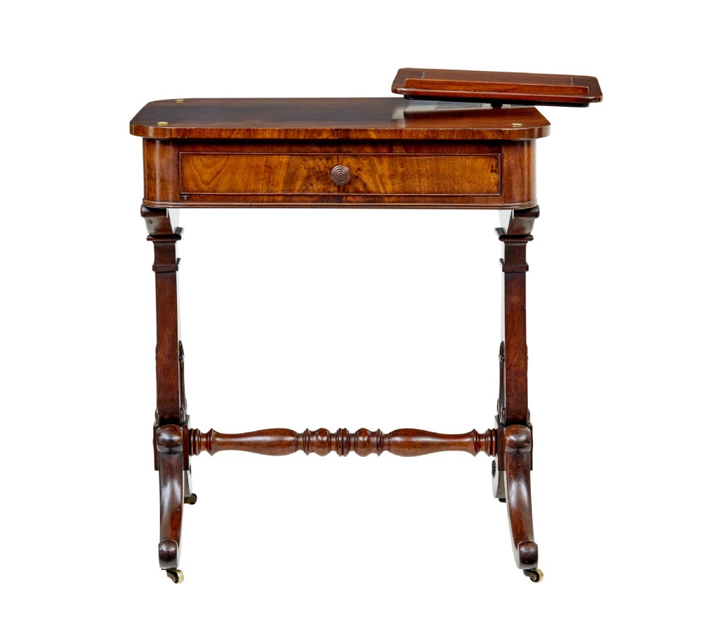 A mid-19th century dark mahogany writing table featuring an adjustable reading slope on top, a single open frieze drawer, scrolled side supports, turned stretcher, and brass castors. View II