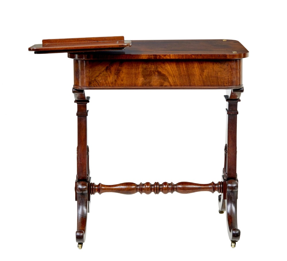 A mid-19th century dark mahogany writing table featuring an adjustable reading slope on top, a single open frieze drawer, scrolled side supports, turned stretcher, and brass castors. View IV