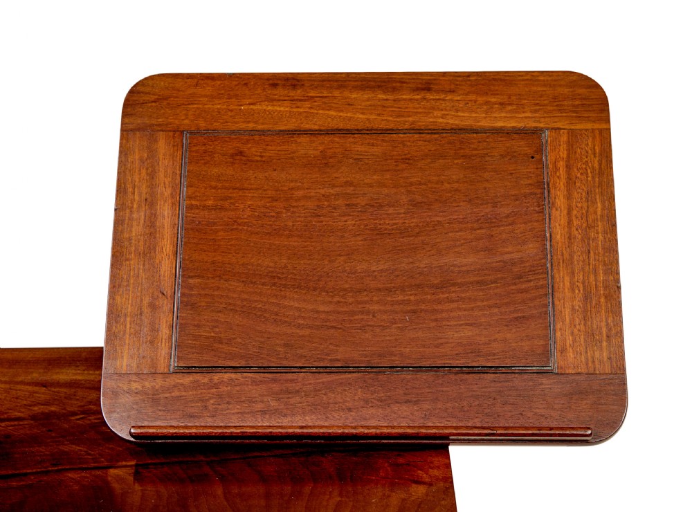A mid-19th century dark mahogany writing table featuring an adjustable reading slope on top, a single open frieze drawer, scrolled side supports, turned stretcher, and brass castors. View V