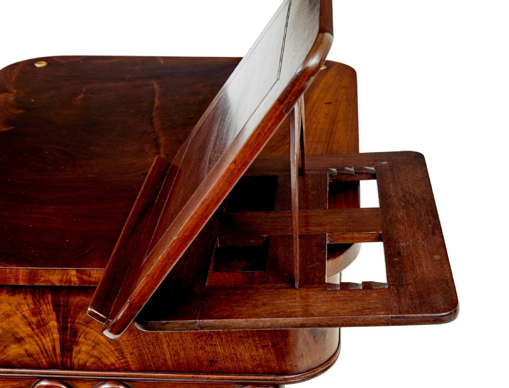 A mid-19th century dark mahogany writing table featuring an adjustable reading slope on top, a single open frieze drawer, scrolled side supports, turned stretcher, and brass castors. View VII