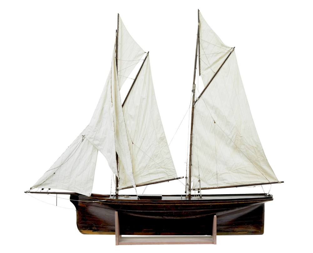 A late 19th-century wooden scale model of a two-masted sailing yacht with off-white sails mounted on a wooden stand.
