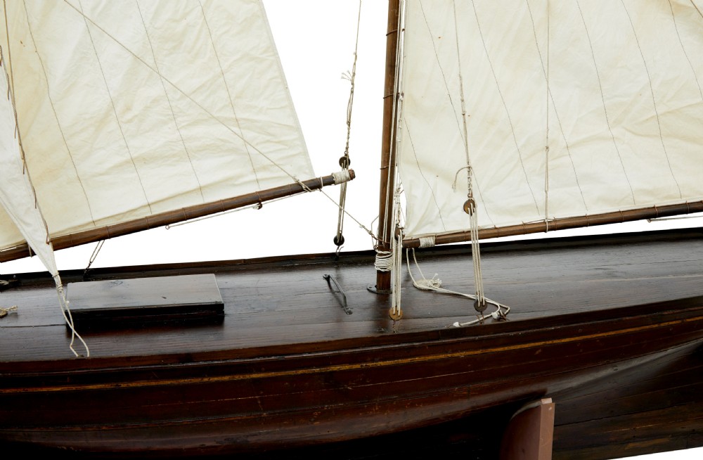 A late 19th-century wooden scale model of a two-masted sailing yacht with off-white sails mounted on a wooden stand. View VII