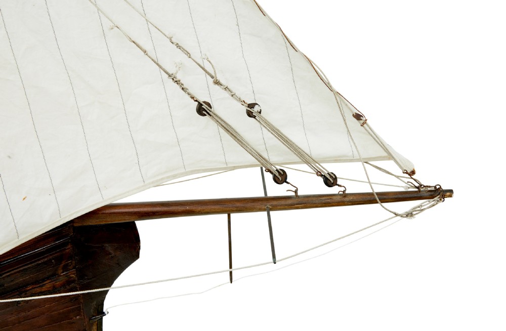 A late 19th-century wooden scale model of a two-masted sailing yacht with off-white sails mounted on a wooden stand. View X