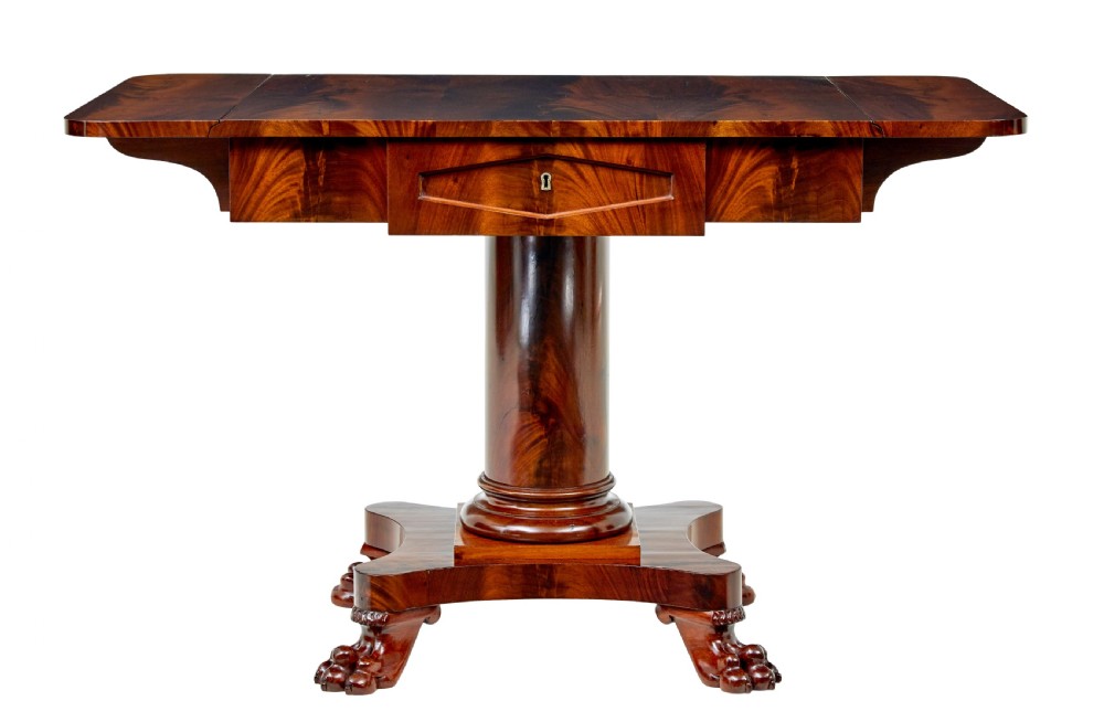 An early 20th-century Scandinavian Empire Revival mahogany sofa table featuring drop leaves, a single frieze drawer, a central cylindrical pedestal, and carved paw feet.