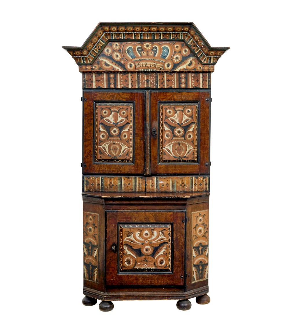 An early nineteenth-century Swedish painted wooden cupboard featuring floral folk art motifs, a shaped cornice dated 1804, and turned bun feet.