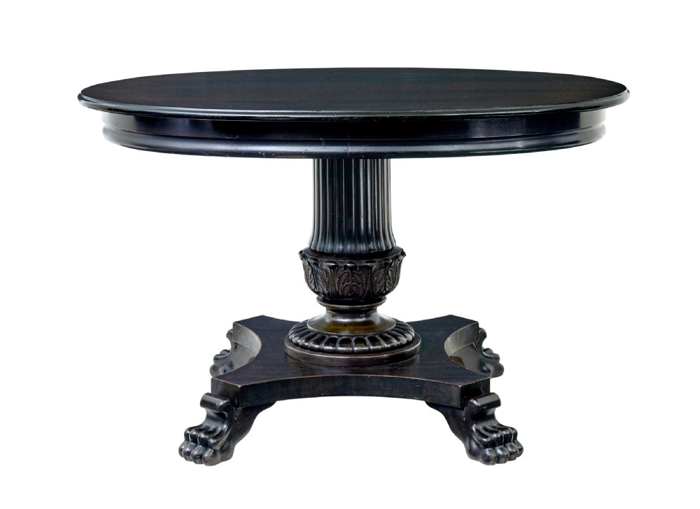 A 19th-century ebonised dark wood oval centre table featuring a fluted central pedestal and a quadform base supported by carved claw feet.