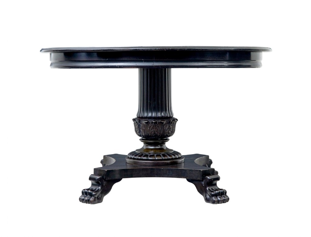 A 19th-century ebonised dark wood oval centre table featuring a fluted central pedestal and a quadform base supported by carved claw feet. View II