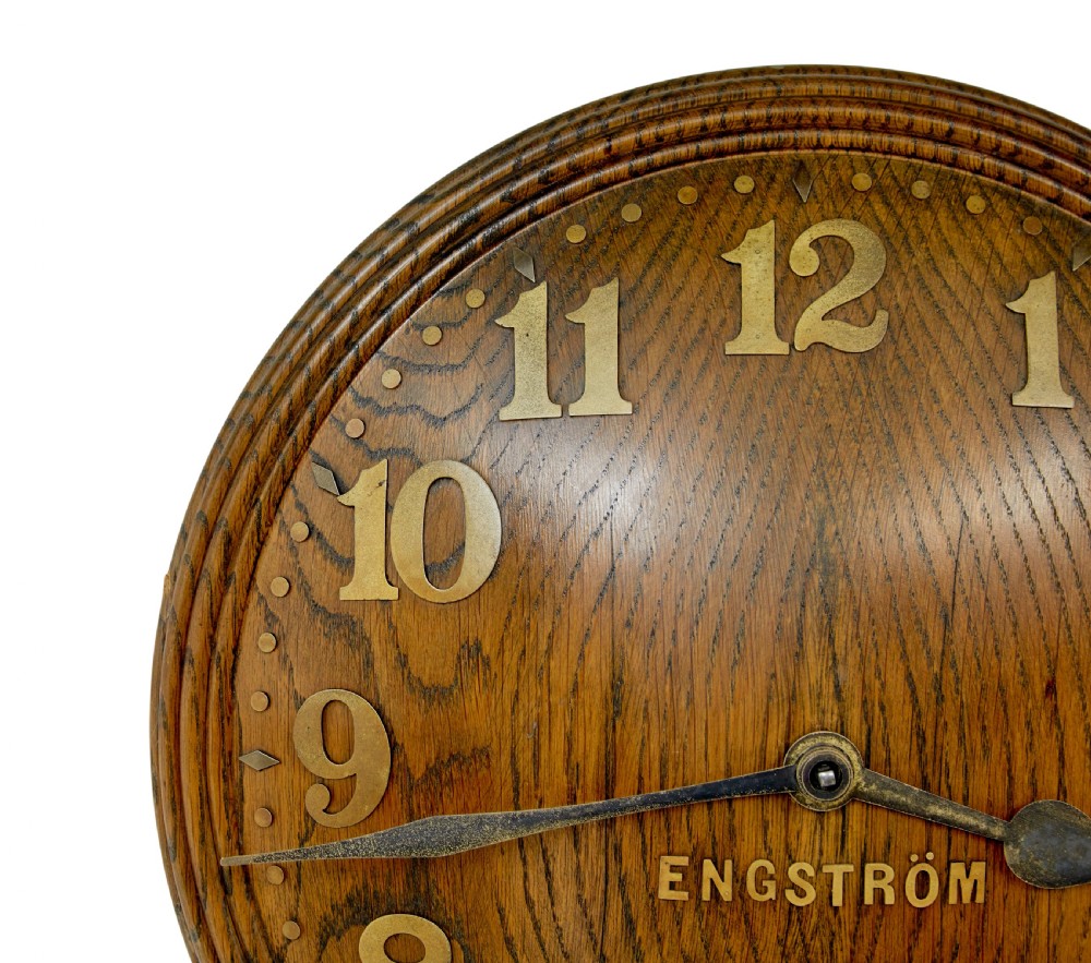 A circular Art Deco wall clock crafted from medium brown oak featuring applied brass Arabic numerals and metallic hands. View II