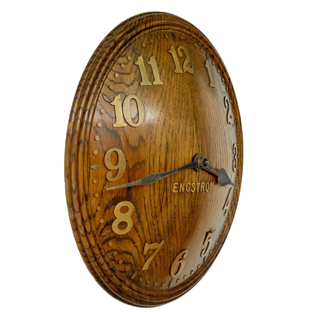 A circular Art Deco wall clock crafted from medium brown oak featuring applied brass Arabic numerals and metallic hands. View IV