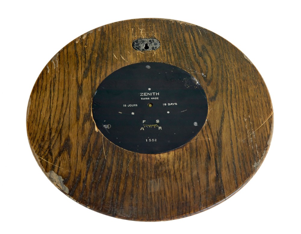 A circular Art Deco wall clock crafted from medium brown oak featuring applied brass Arabic numerals and metallic hands. View V