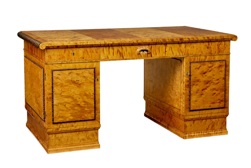 An Art Deco twin-pedestalled desk crafted from golden flame birch veneer featuring multiple drawers, cupboard doors, and decorative reeded borders.
