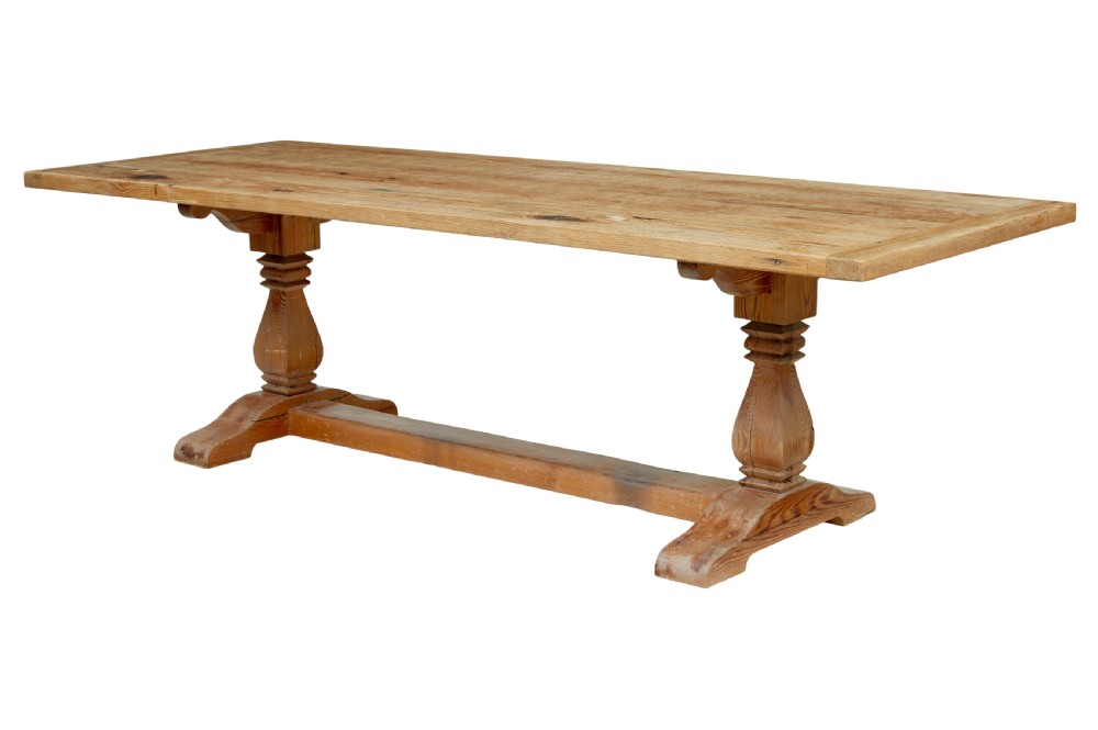 A nineteenth-century pine refectory dining table featuring a plank top, carved baluster supports, and a low central floor stretcher.