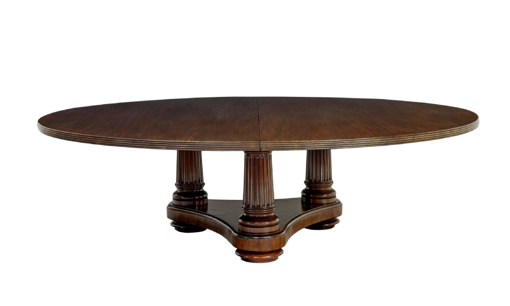 A mid 19th-century mahogany dining table featuring a broad oval top supported by three fluted column pedestals on a tri-form platform base. View II