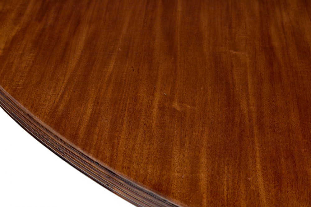A mid 19th-century mahogany dining table featuring a broad oval top supported by three fluted column pedestals on a tri-form platform base. View IV