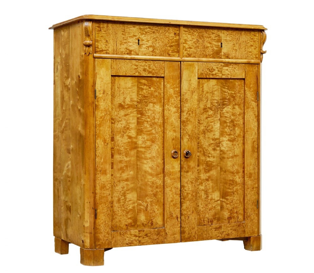 A nineteenth-century Swedish two-door cupboard constructed from golden tiger birch wood with two upper drawers and carved corner corbels.