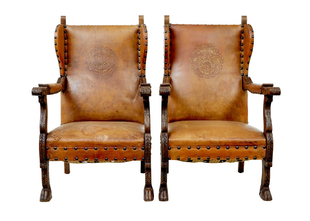 A pair of 19th-century oak armchairs featuring tan leather upholstery with central embossed medallions, brass stud trim, and carved supports.