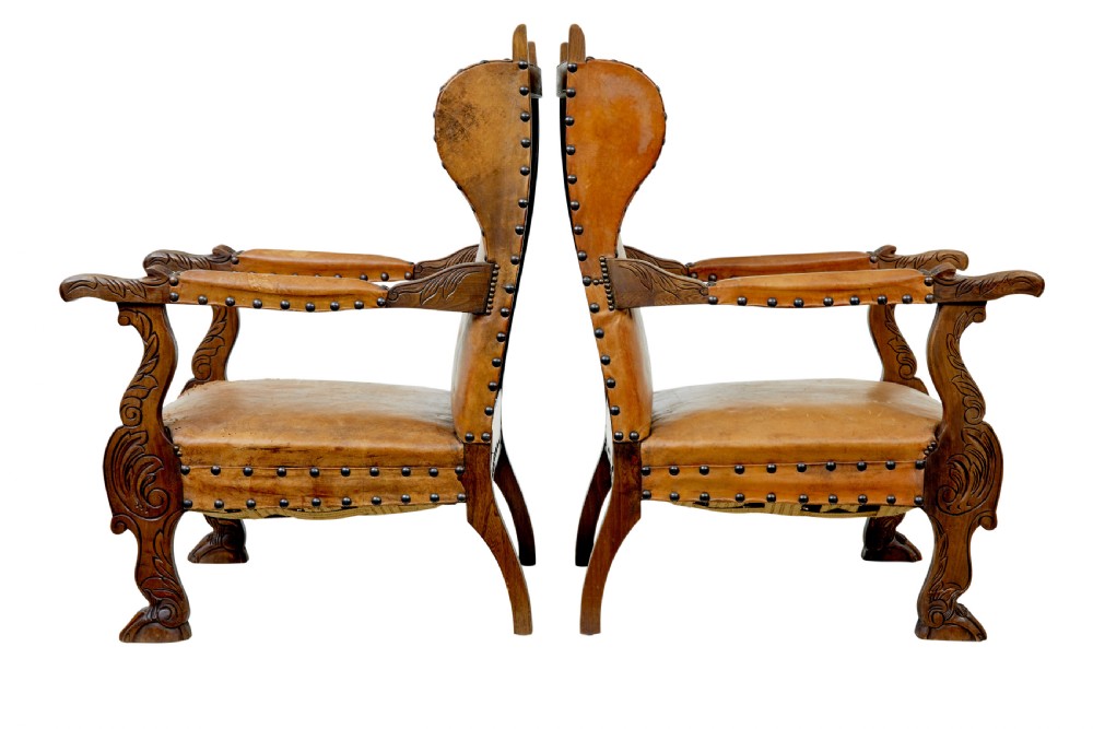 A pair of 19th-century oak armchairs featuring tan leather upholstery with central embossed medallions, brass stud trim, and carved supports. View II