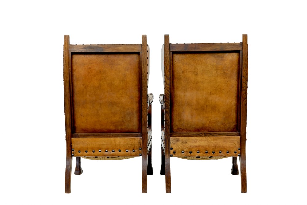 A pair of 19th-century oak armchairs featuring tan leather upholstery with central embossed medallions, brass stud trim, and carved supports. View IV
