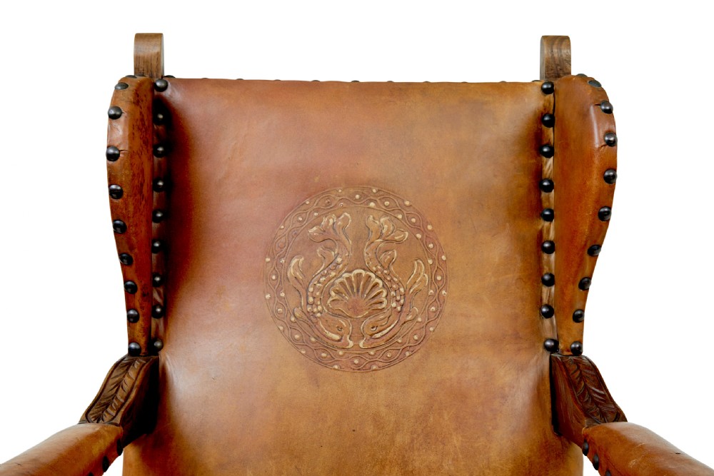 A pair of 19th-century oak armchairs featuring tan leather upholstery with central embossed medallions, brass stud trim, and carved supports. View VI