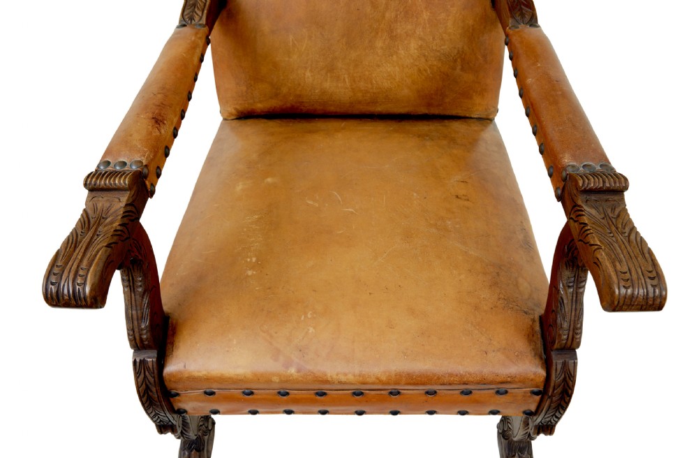 A pair of 19th-century oak armchairs featuring tan leather upholstery with central embossed medallions, brass stud trim, and carved supports. View VII