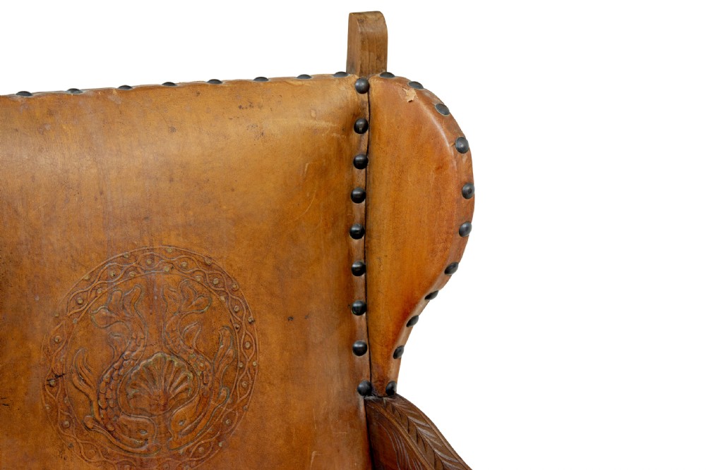 A pair of 19th-century oak armchairs featuring tan leather upholstery with central embossed medallions, brass stud trim, and carved supports. View IX