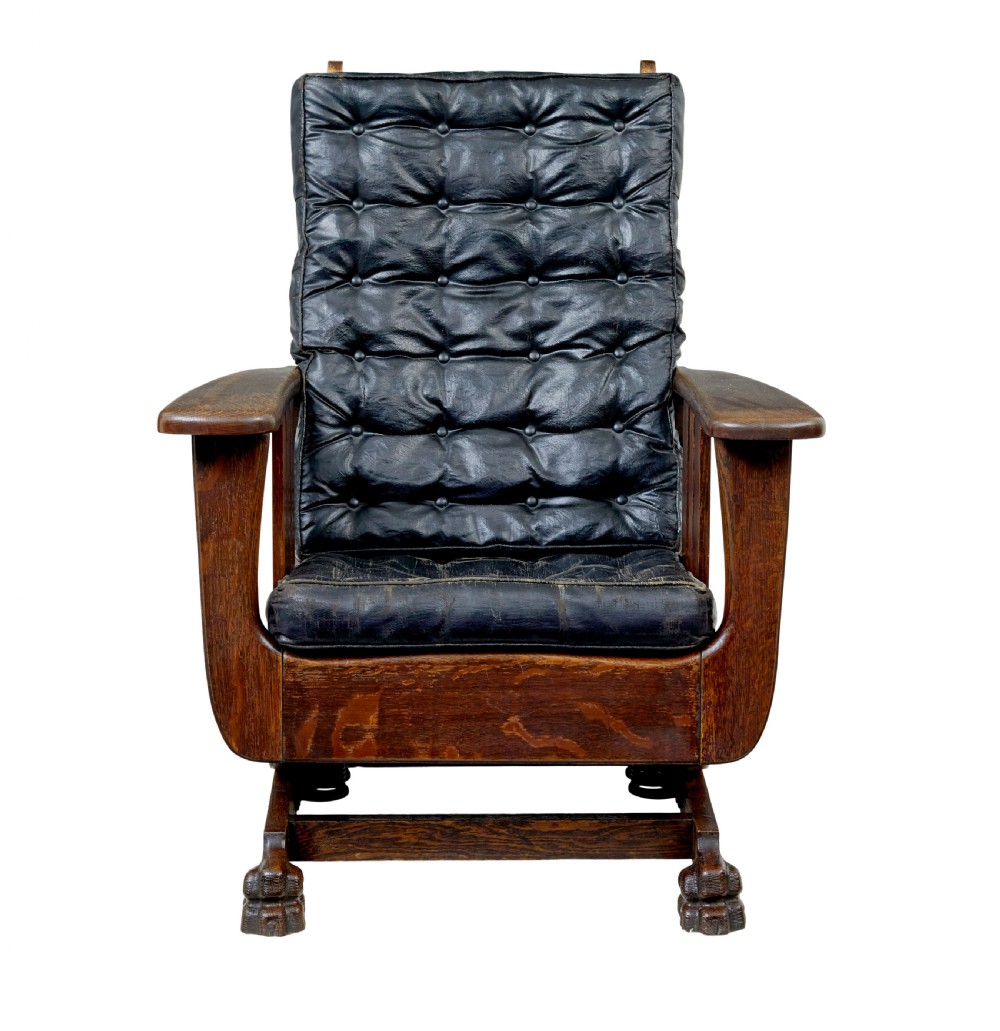 An early 20th-century dark oak platform rocking chair featuring button-tufted black leather cushions and carved front feet. View II