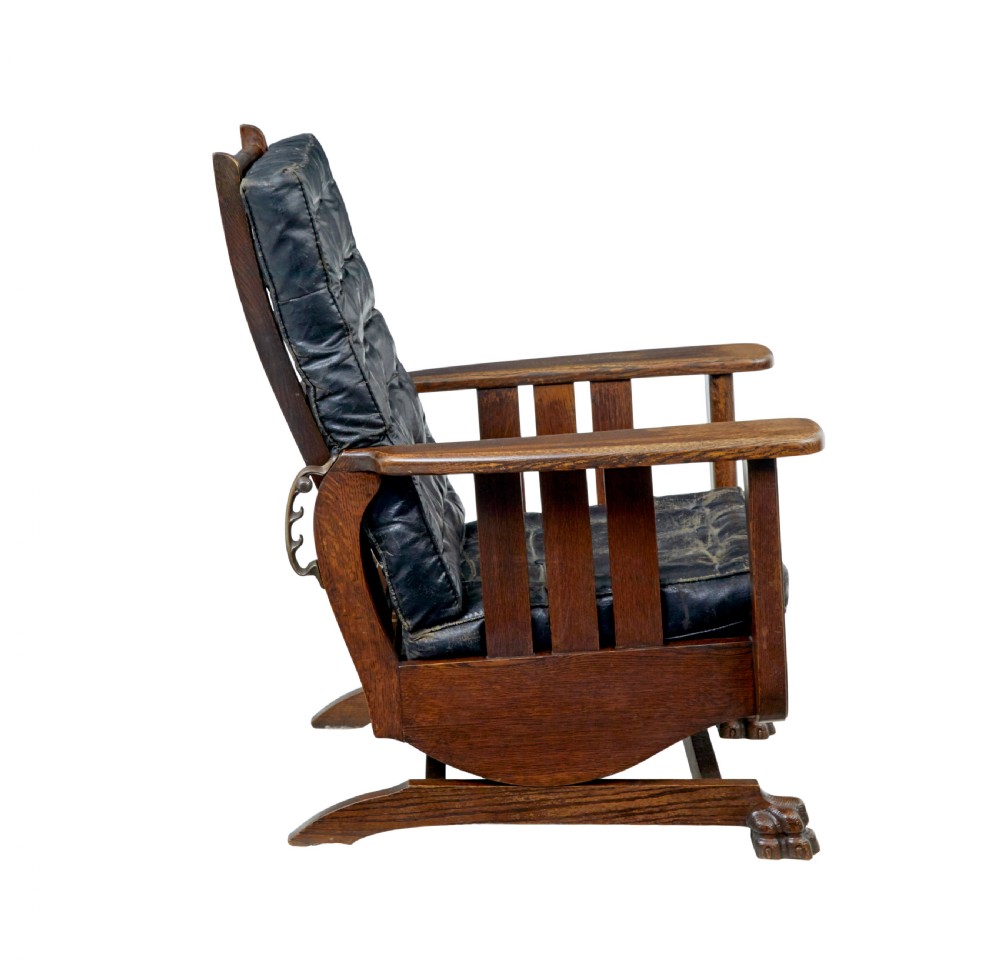 An early 20th-century dark oak platform rocking chair featuring button-tufted black leather cushions and carved front feet. View V